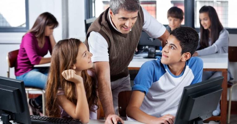 A teacher helping two students at their desk in a classroom