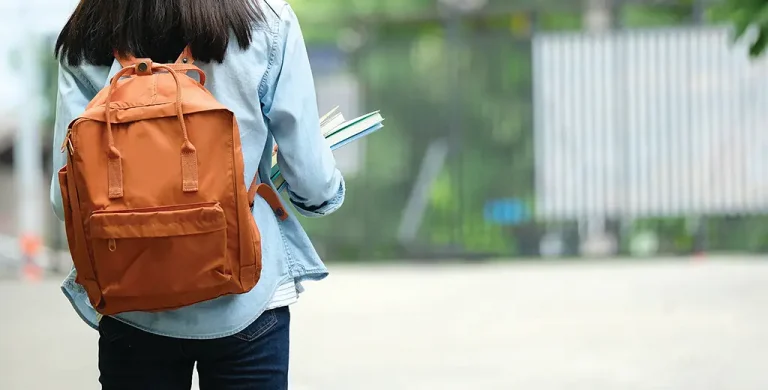 Teenager on campus walking to class with backpack and books.