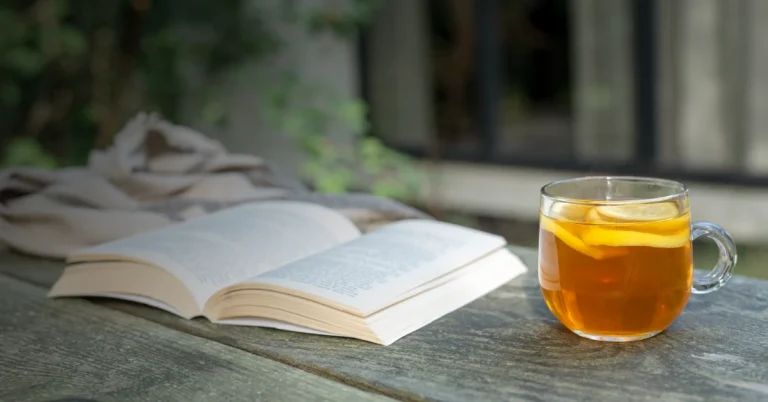 A textbook and a cup of coffee lay atop a lakeside dock on a summer morning.