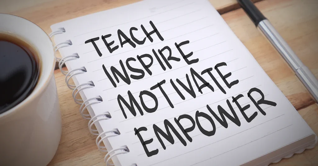 An open notebook sits on a table next to a cup of coffee with the words teach, inspire, motivate, and empower written on it.