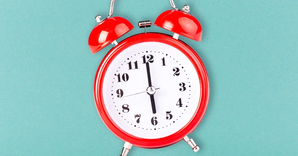 A clock hand ticks down the seconds on a red alarm clock.