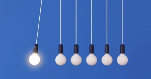 A mock up of hanging light bulbs with one glowing on a blue wall background swings like a conceptual idea of a pendulum.