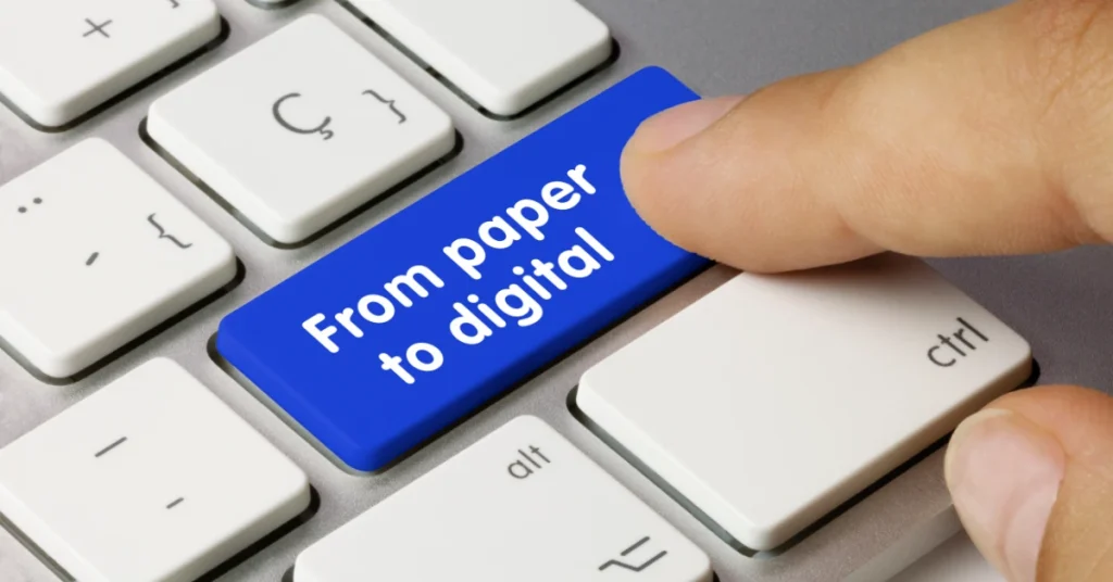 A finger presses down on a blue button that says “From paper to digital” that is part of a silver computer keyboard.