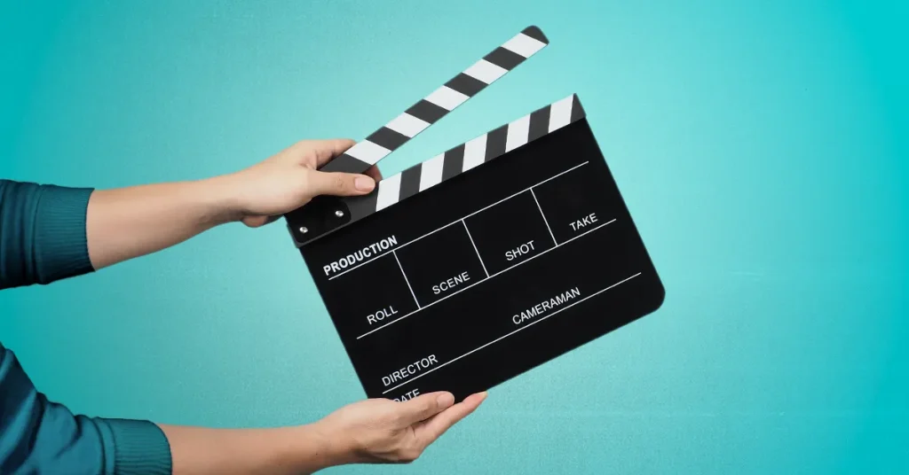 A hand is holding a black movie slate on a mint green background.