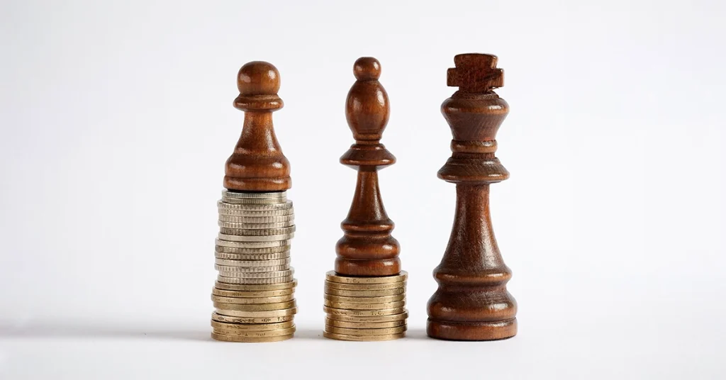 Three chess pieces stand on equitable ground built made up of stacks of coins.