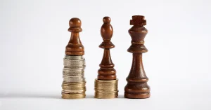 Three chess pieces stand on equitable ground built made up of stacks of coins.