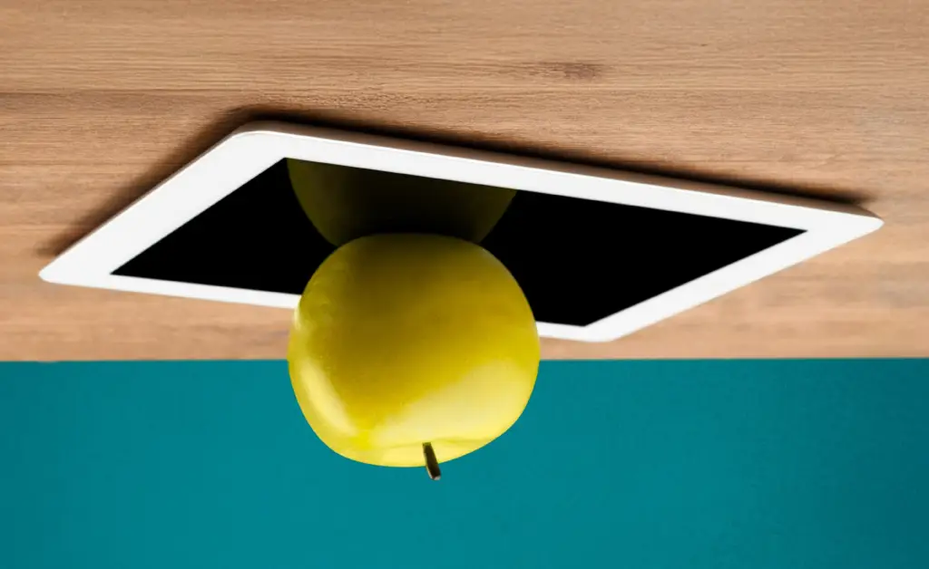 A yellow apple sits atop a tablet, upside down, on an upside-down desk