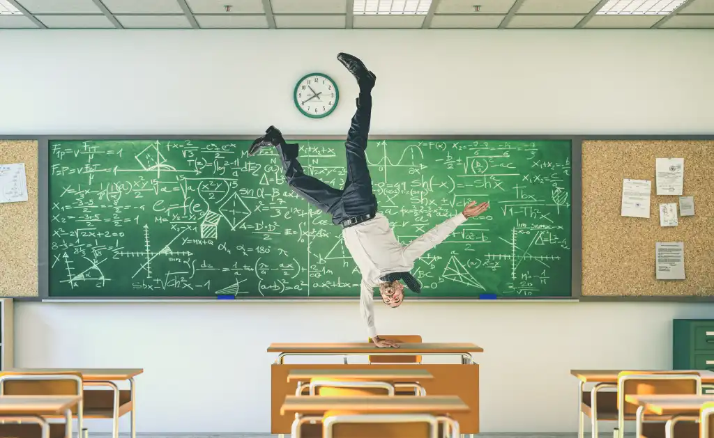 A teacher balances upside down on a desk in a classroom.