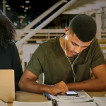 A group of high school students study together with their notes and devices in a library.