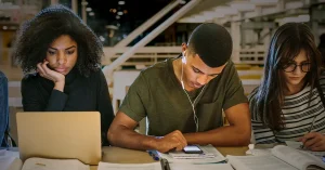 A group of high school students study together with their notes and devices in a library.