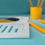 A student data report sits on a turquoise desk next to some yellow pencils.