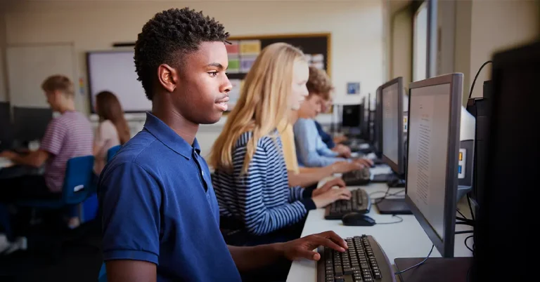 A line of male and female high school students sitting at computers taking the AP exam.