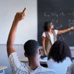 Image showing the Student raising a hand to ask a question in class while the teacher is explaining