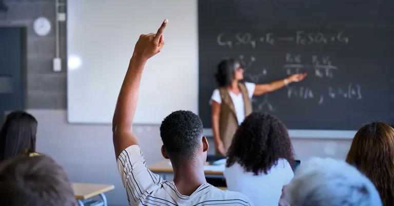 Image showing the Student raising a hand to ask a question in class while the teacher is explaining